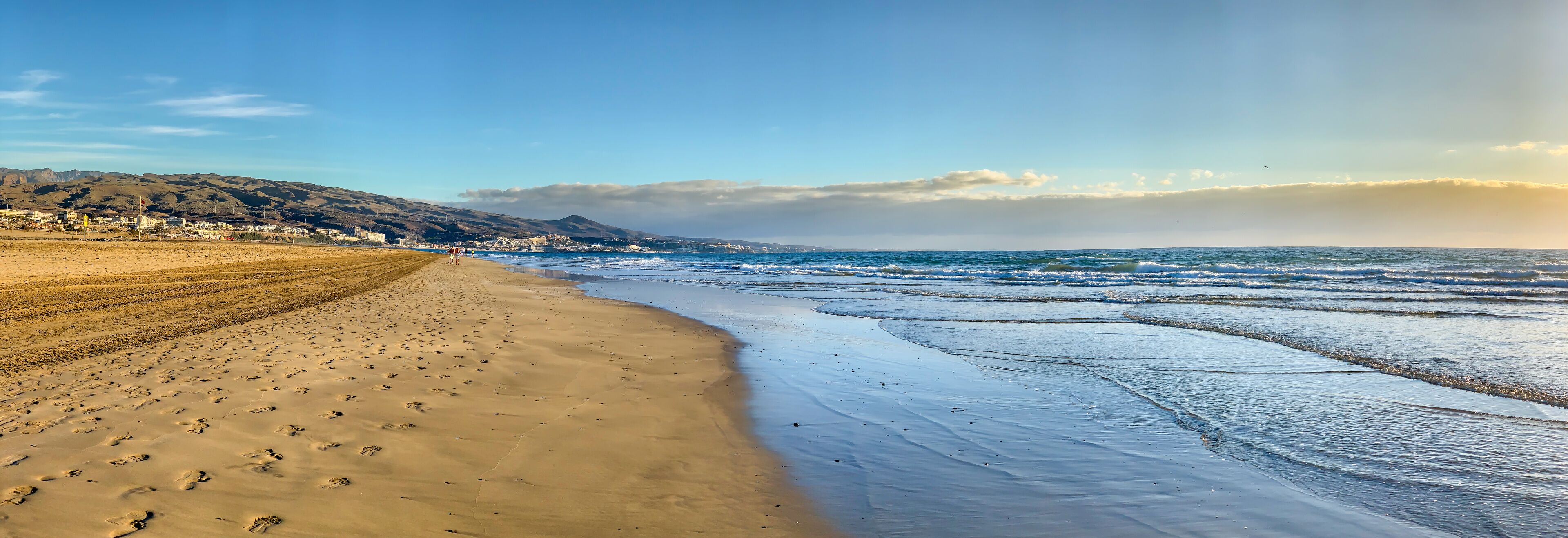 A beach with footprints, waves, and a distant cityscape.