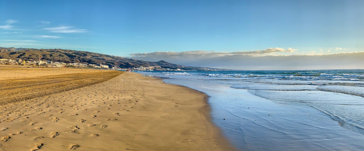 A beach with footprints, waves, and a distant cityscape.