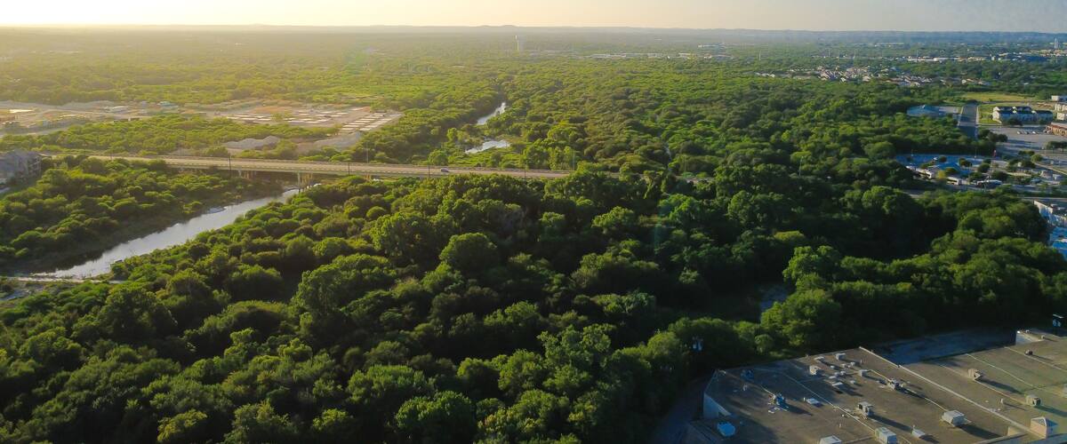 Un paysage verdoyant et luxuriant, avec une rivière, un pont et une éolienne visible au loin.