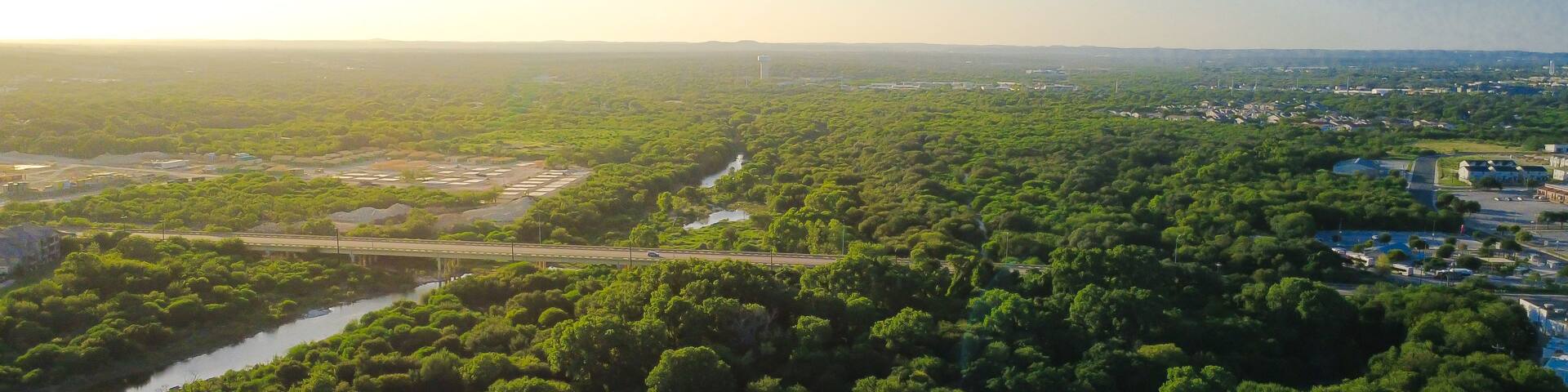 A lush green landscape with a river, a bridge, and a distant wind turbine.