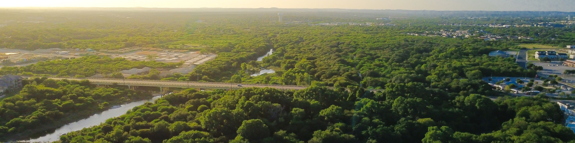 Un paisaje exuberante y verde con un río, un puente y una turbina eólica a lo lejos.