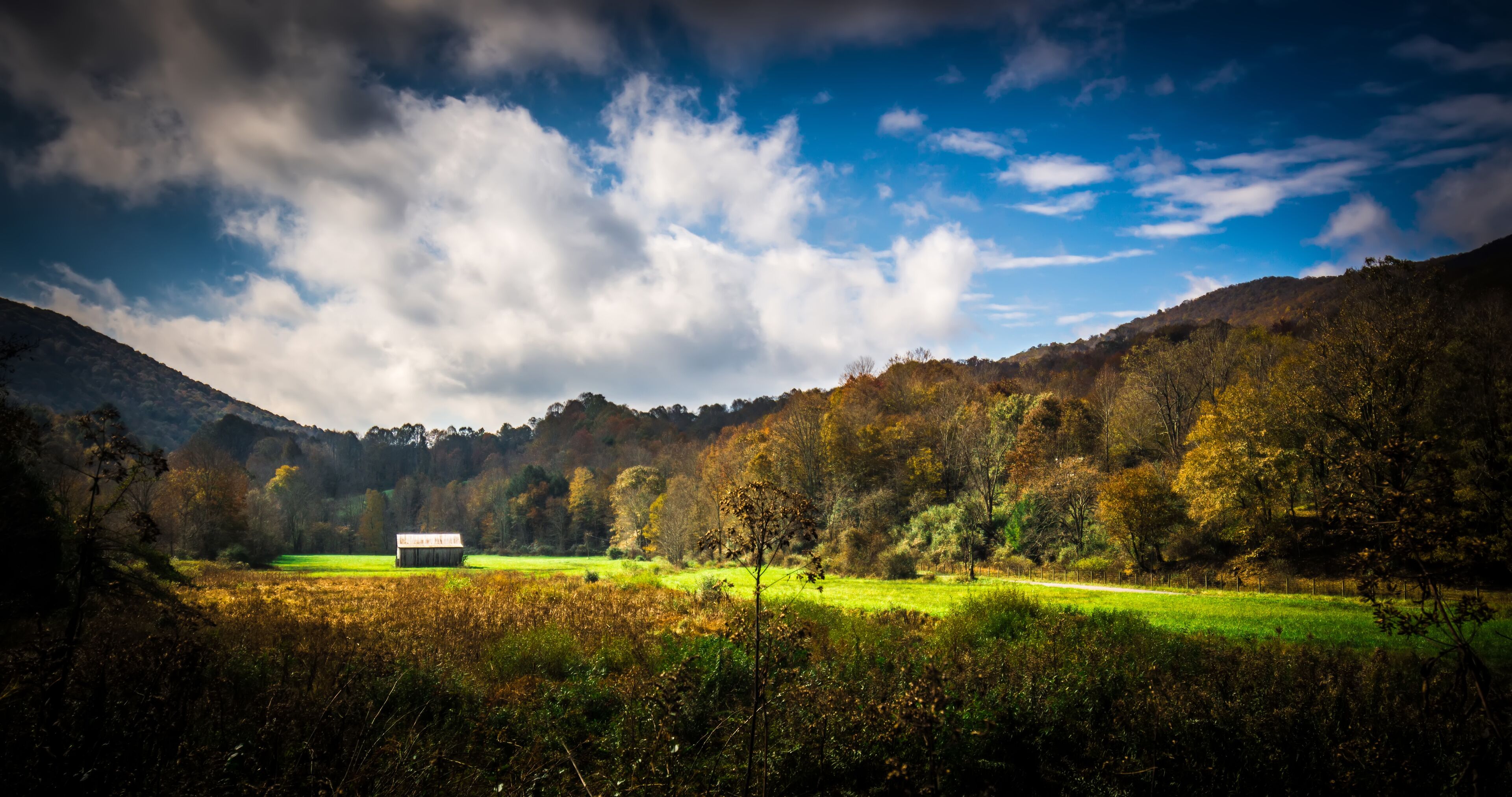 A rural landscape with a barn in the foreground, rolling hills, and a partly cloudy sky.