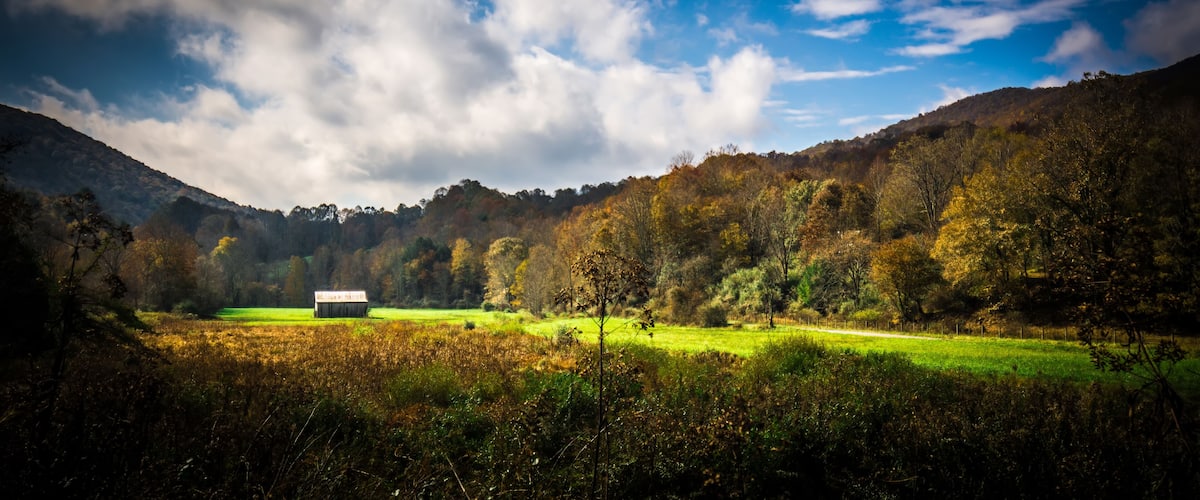 A rural landscape with a barn in the foreground, rolling hills, and a partly cloudy sky.