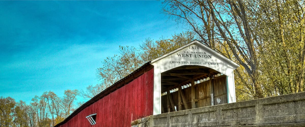 A red covered bridge with a sign reading "1876 J.J. Daniel's West Union" and "Cross this bridge at a walk".