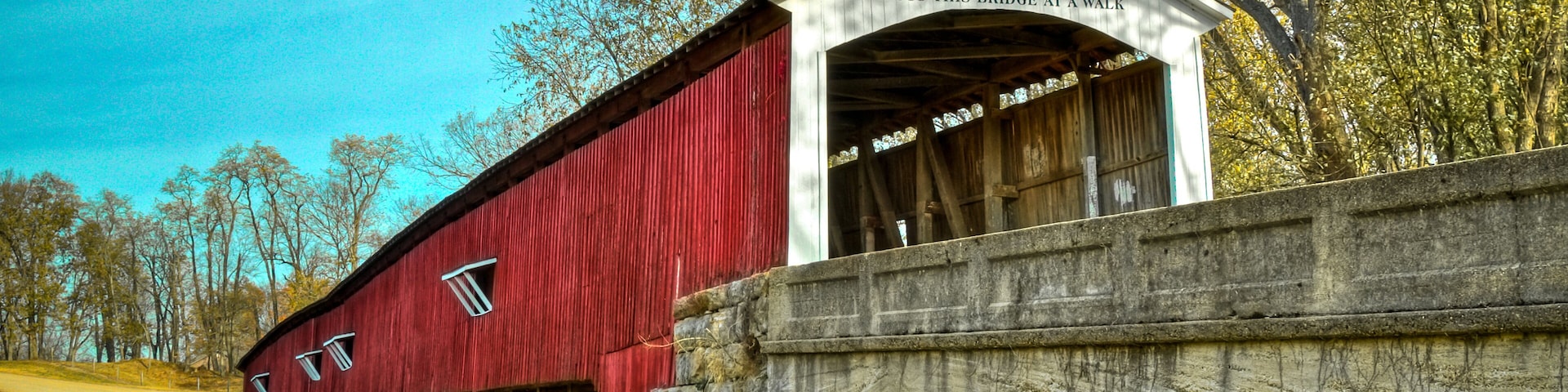 A red covered bridge with a sign reading "1876 J.J. Daniel's West Union" and "Cross this bridge at a walk".