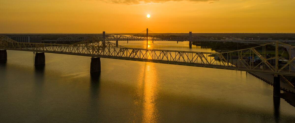 A bridge over a body of water with the sun setting in the background.