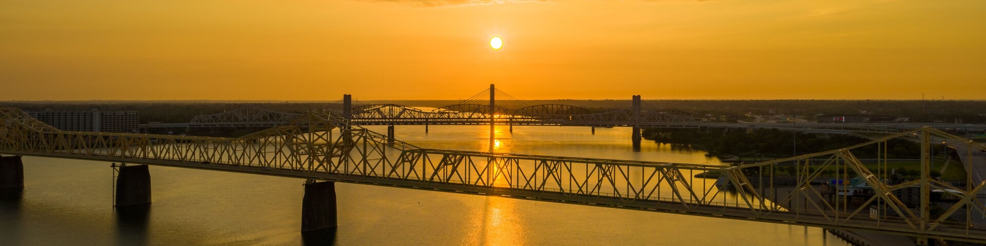 Eine Brücke über dem Wasser, im Hintergrund geht die Sonne unter.