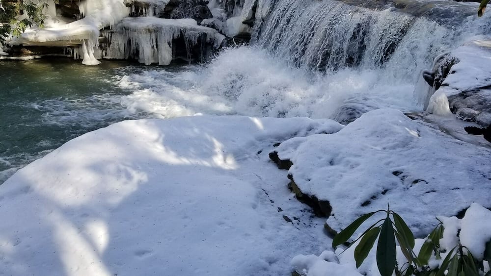 A snow-covered waterfall in a forested area.
