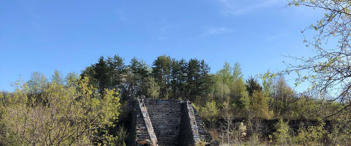A rural landscape with a dilapidated stone structure, a dirt path, and surrounding greenery.