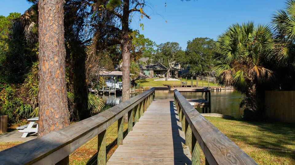 A wooden boardwalk leading to a dock with boats, surrounded by trees and a grassy area.