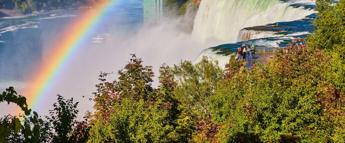 A waterfall with a rainbow, a bridge, and lush greenery.