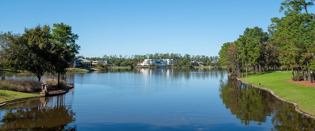 Ein ruhiger See mit Spiegelung des Himmels, umgeben von Bäumen und einem Golfplatz.