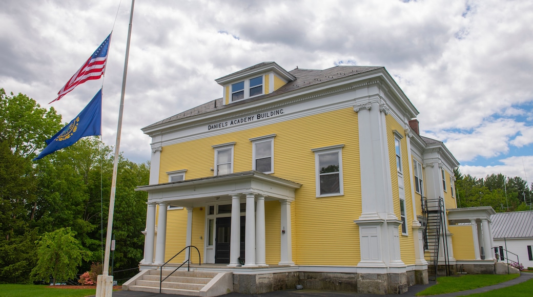 Ein gelbes Gebäude mit der Aufschrift 'DANIELS ACADEMY BUILDING' an der Fassade, eine Fahnenmast mit einer US-amerikanischen Flagge und eine blaue Flagge mit goldenen Verzierungen.