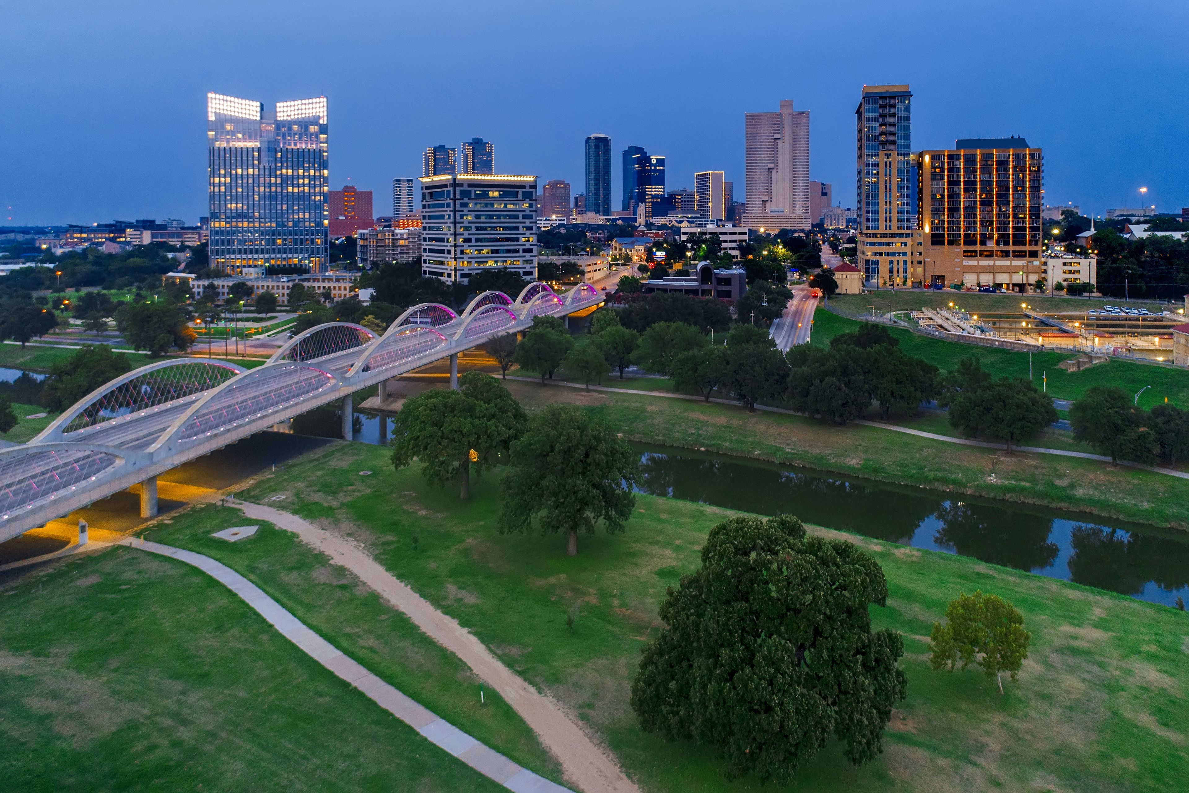A city skyline with modern buildings and a pedestrian bridge over a river.