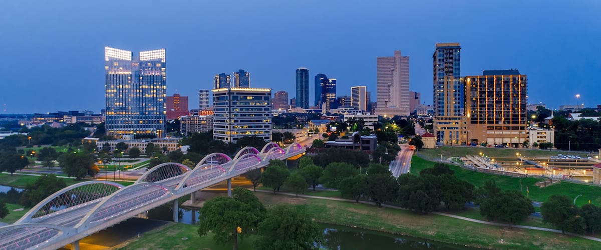 A city skyline with modern buildings and a pedestrian bridge over a river.
