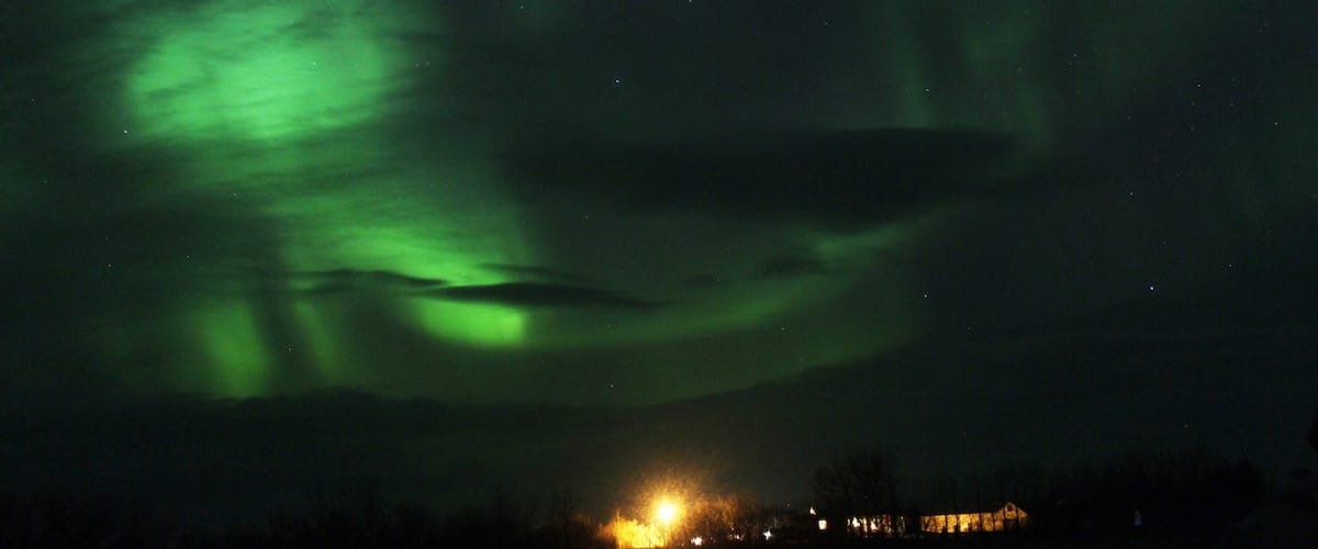The Northern Lights over a dark sky with a faintly lit building at the bottom.