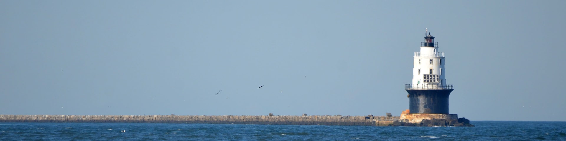 Un faro junto al mar, con olas rompiendo al frente.