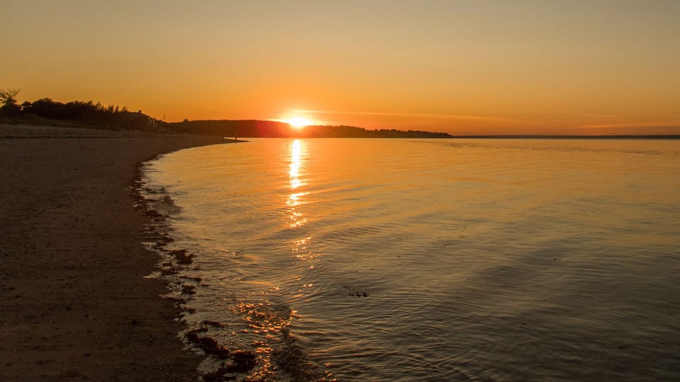 A sunset over a calm beach with gentle waves lapping at the shore.