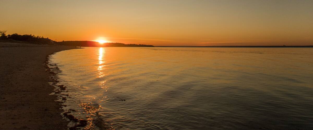 A sunset over a calm beach with gentle waves lapping at the shore.