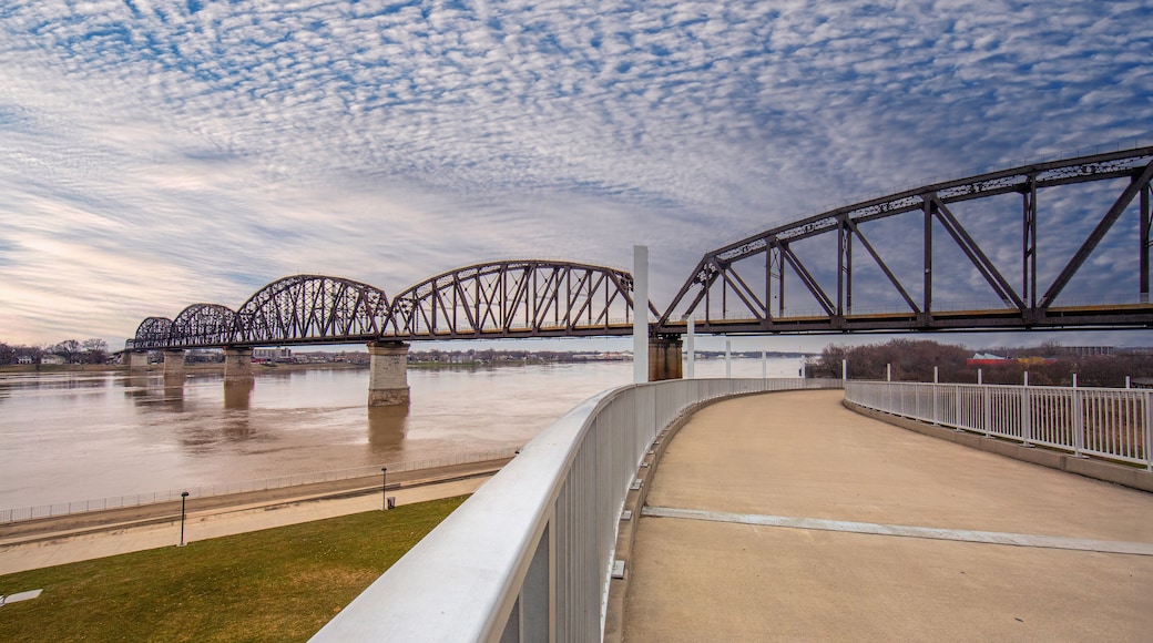 A steel bridge with multiple arches over a river, a concrete viewing platform, and a cloudy sky.