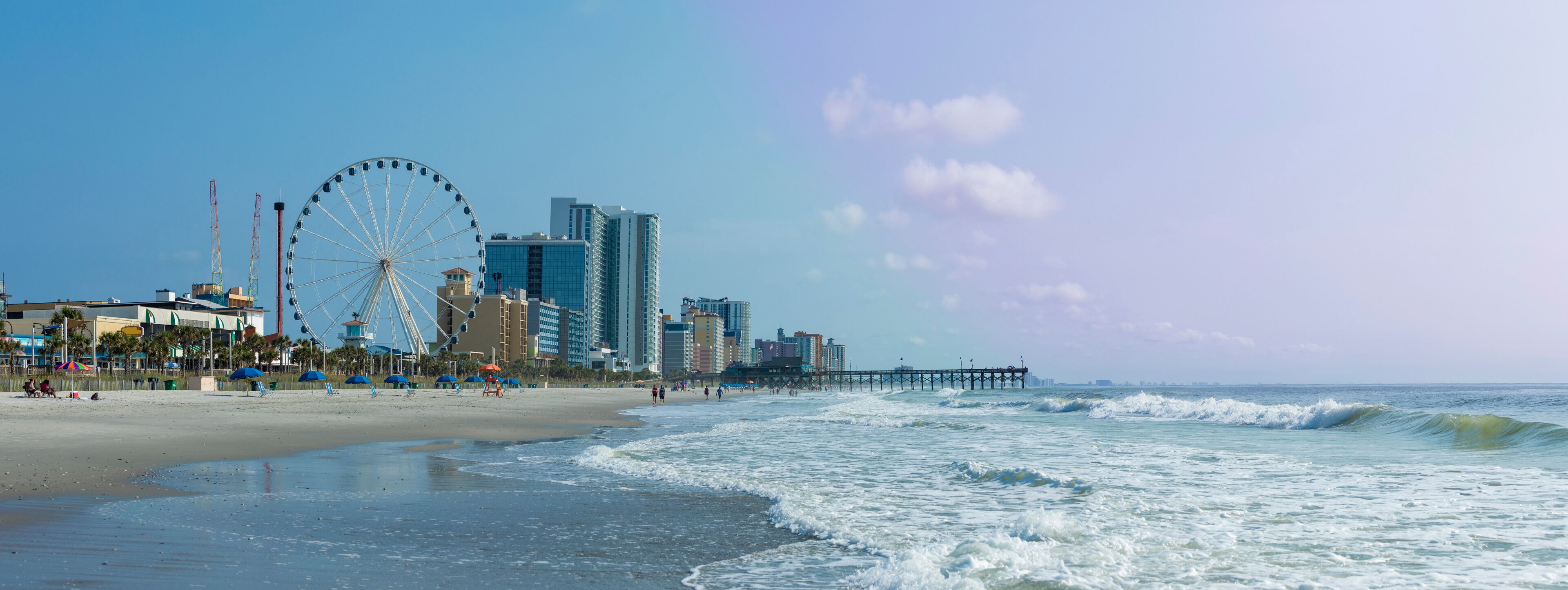 A beach with a Ferris wheel, a pier, and modern buildings.