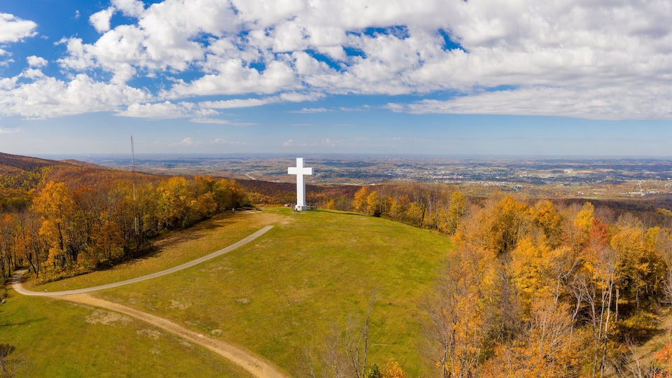 A cross on a hill with autumn foliage and a view of a valley.