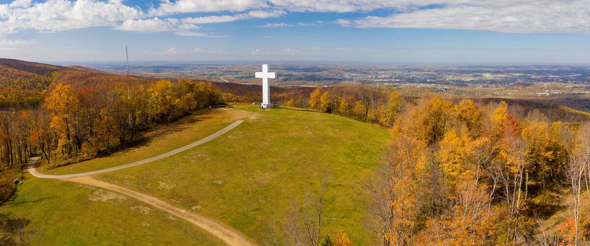 A cross on a hill with autumn foliage and a view of a valley.