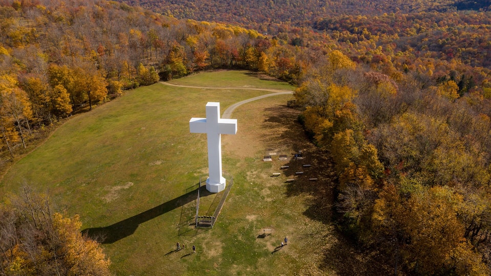 A large white cross surrounded by a grassy field and autumn-colored trees.