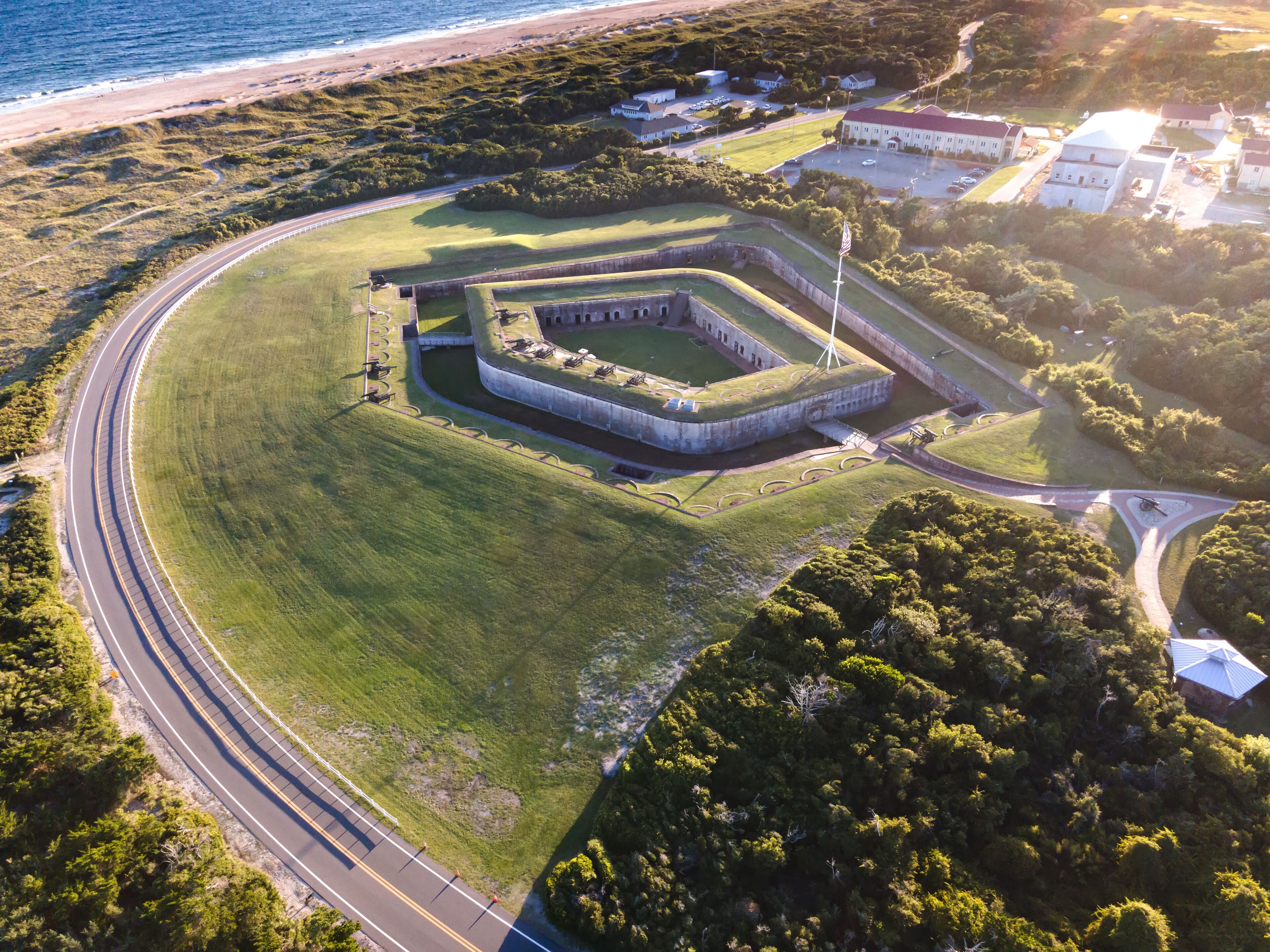 An aerial view of a coastal fort with a surrounding road and greenery.