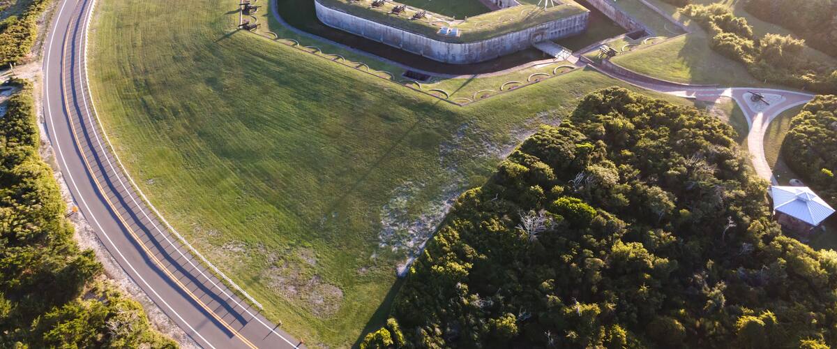 An aerial view of a coastal fort with a surrounding road and greenery.