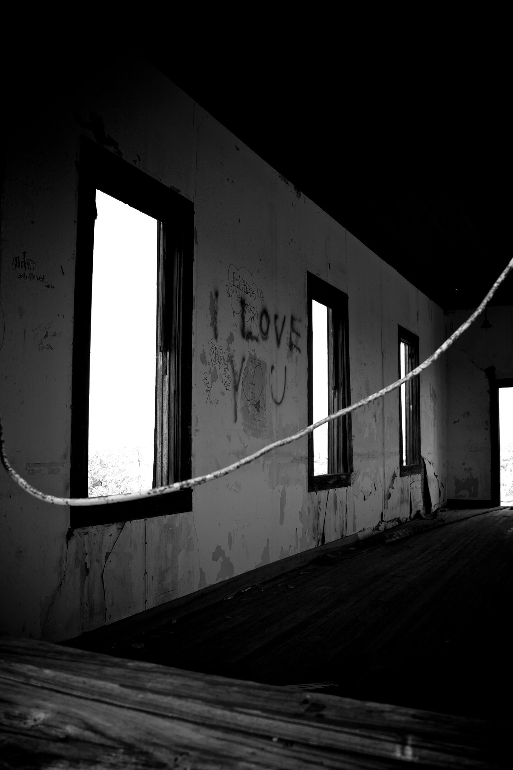 An abandoned building with graffiti, including 'I LOVE YOU' on the wall, and a rope across the room.