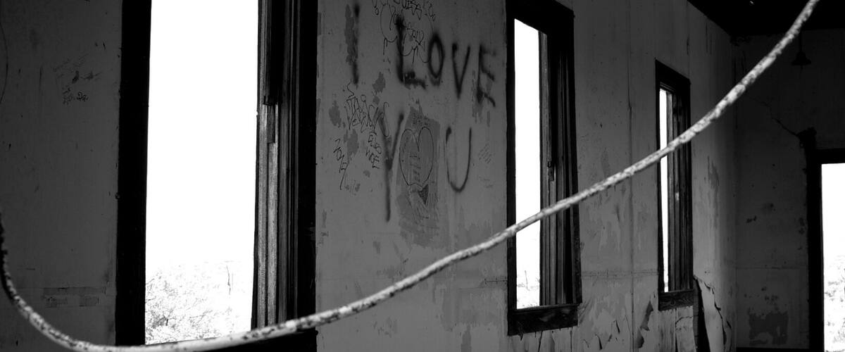 An abandoned building with graffiti, including 'I LOVE YOU' on the wall, and a rope across the room.
