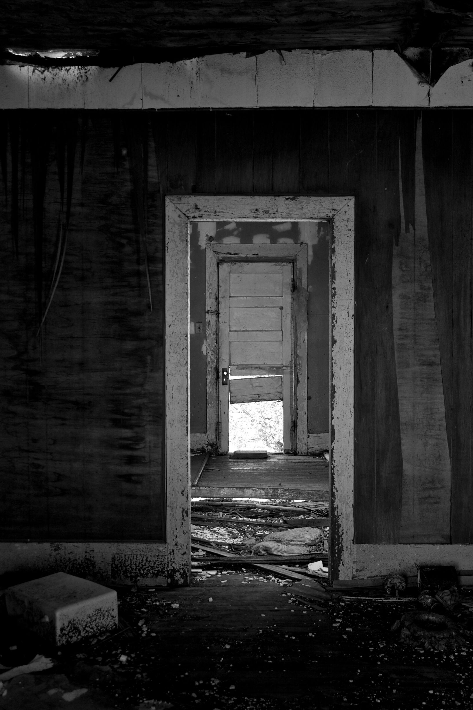 An abandoned building with a doorway leading to a brighter interior.