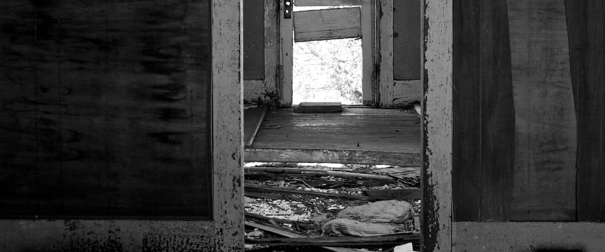 An abandoned building with a doorway leading to a brighter interior.