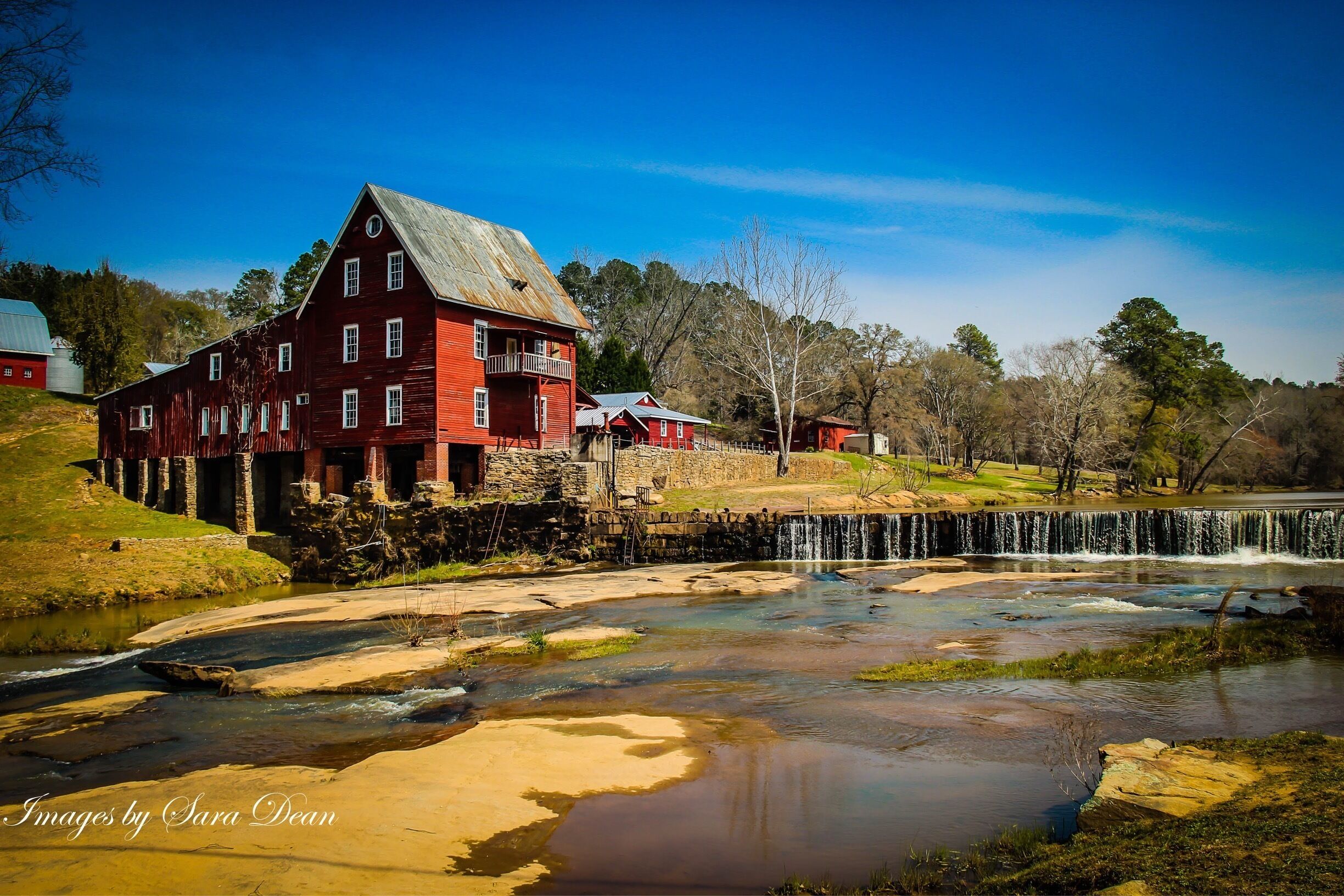 A red barn with a stone foundation, a small waterfall, and a clear blue sky.