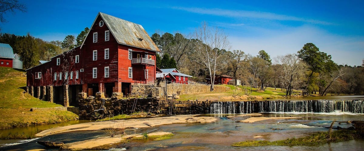 A red barn with a stone foundation, a small waterfall, and a clear blue sky.