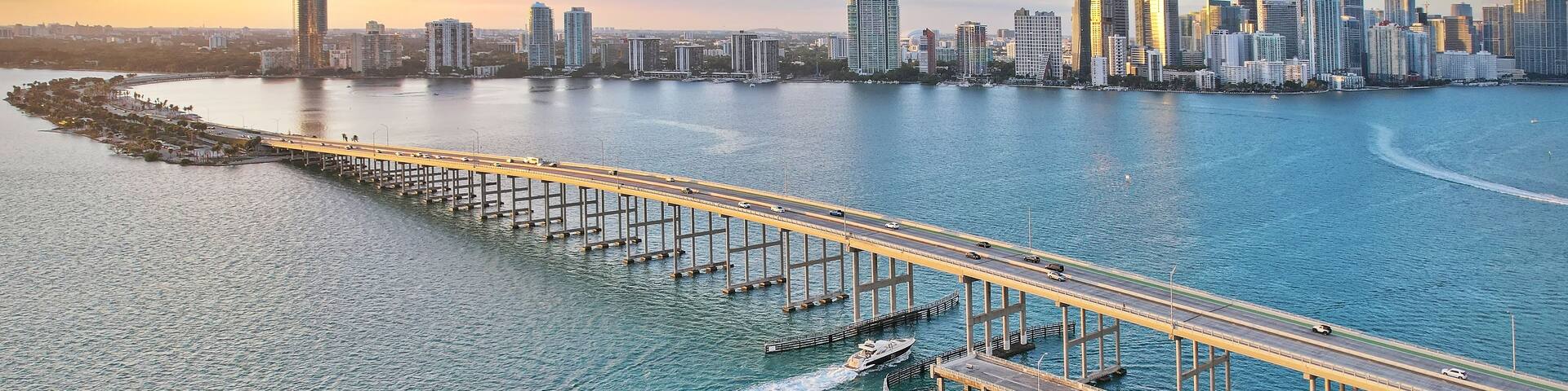 A coastal cityscape with a prominent bridge extending into the water, surrounded by high-rise buildings.