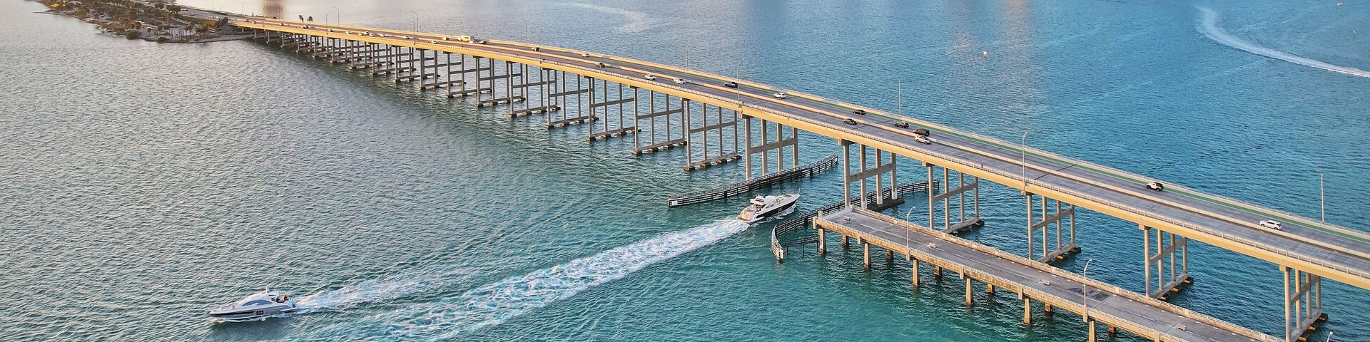 Un paisaje urbano costero con un puente destacado que se extiende sobre el agua, rodeado de edificios altos.