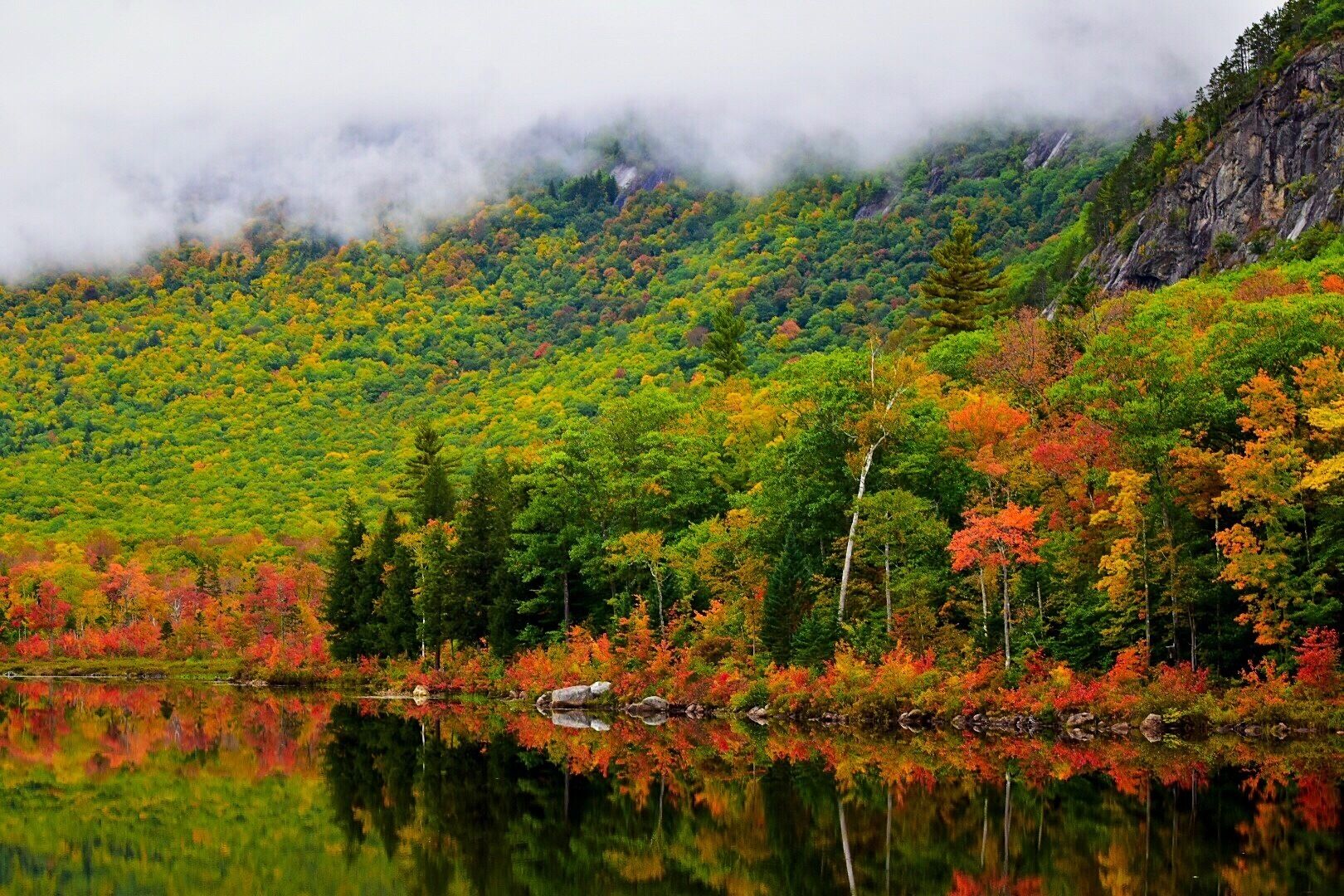 A mountain landscape with autumn foliage reflecting in a calm lake.