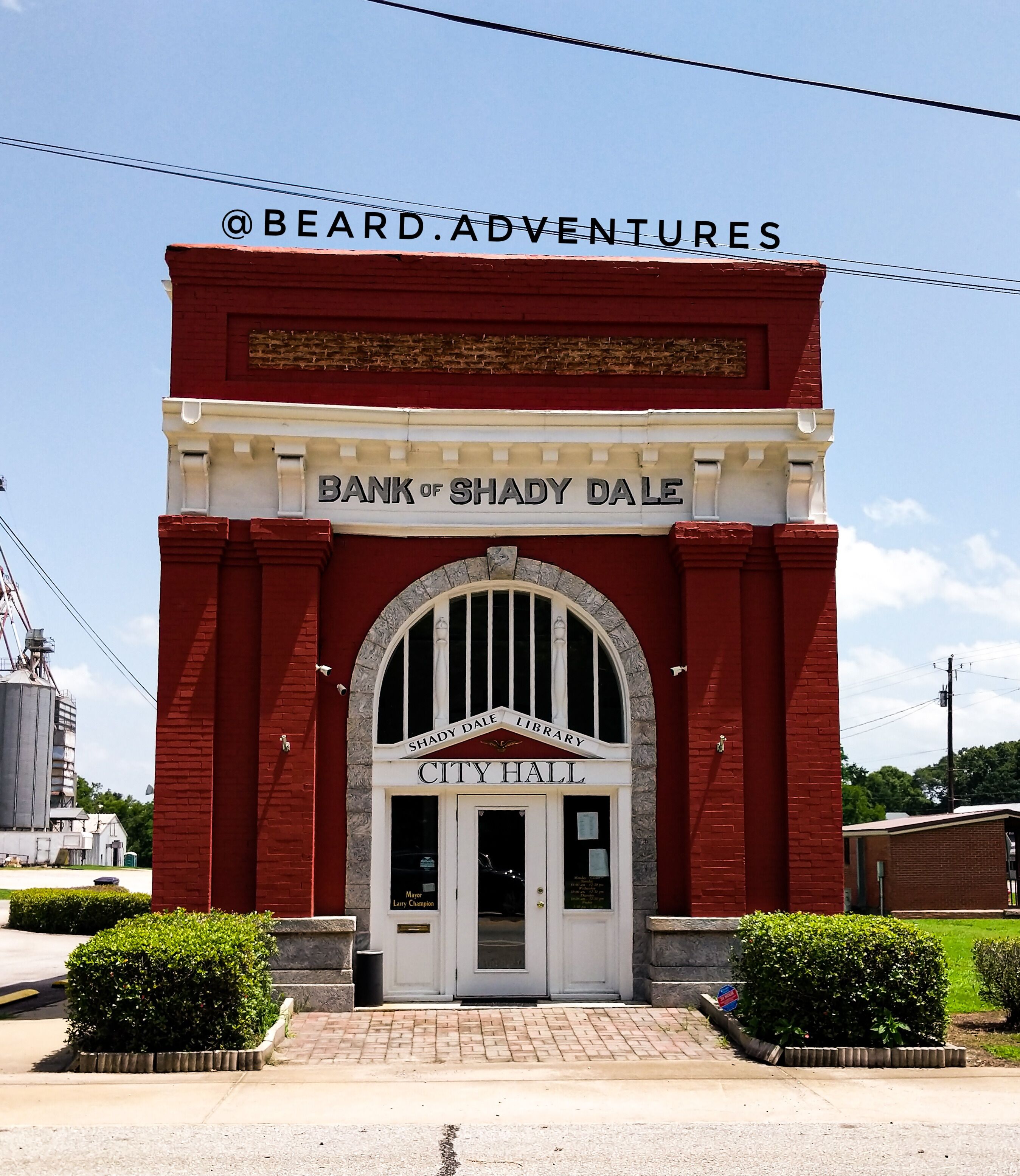 A red brick building with a white archway labeled "City Hall" and "Bank of Shady Dale Library" above it.