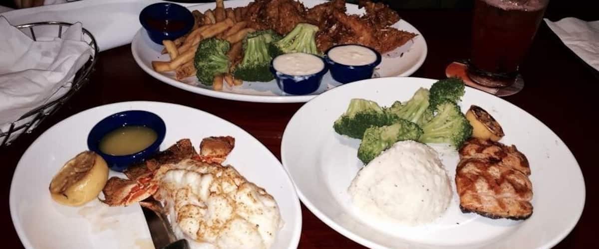 A table with plates of food including fish, potatoes, and broccoli.