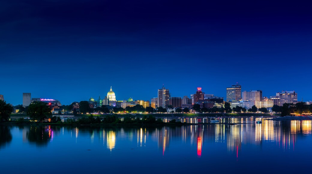 A city skyline at night with illuminated buildings reflecting on a calm body of water.