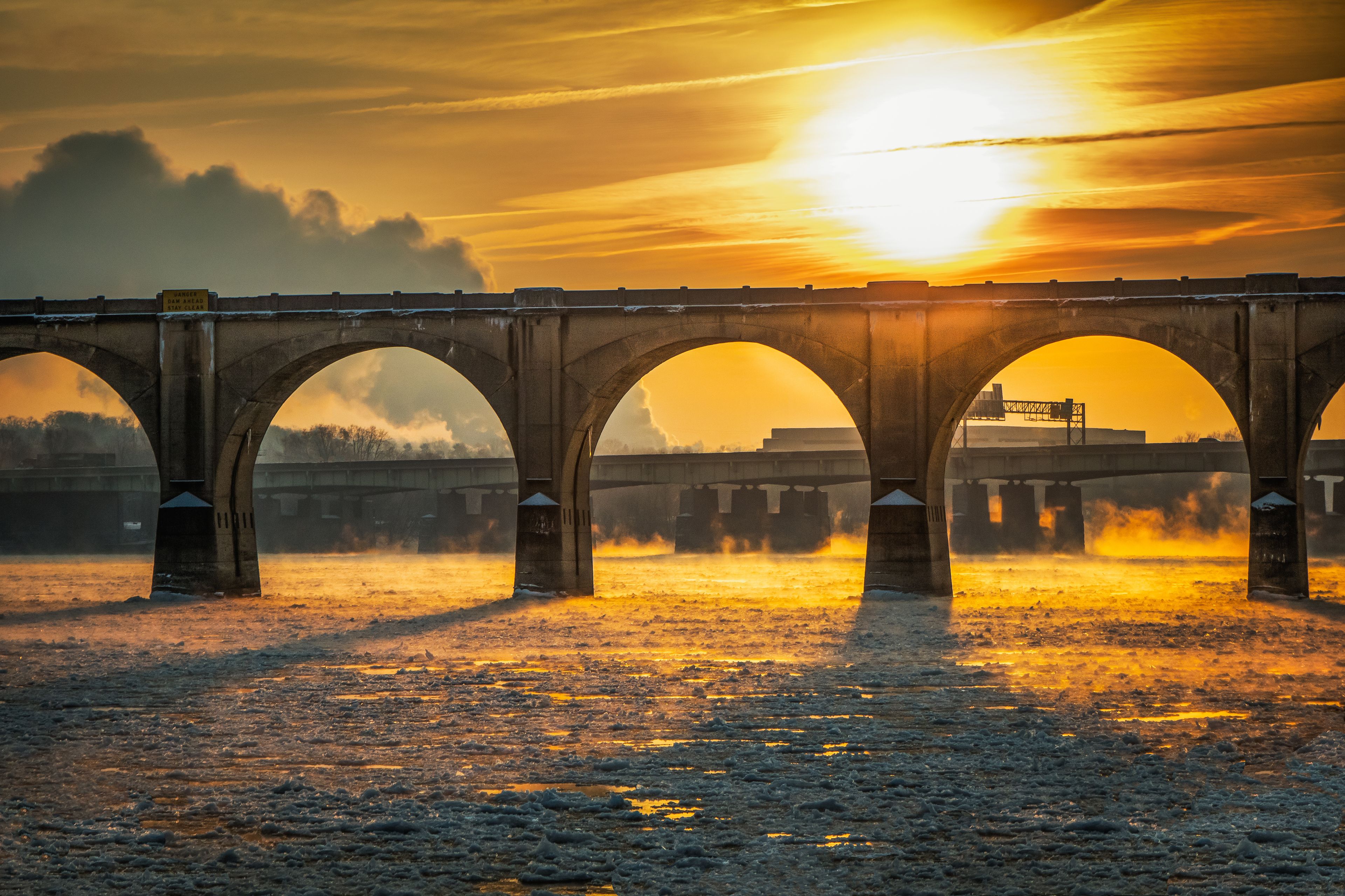 A bridge with multiple arches over a body of water during sunset.