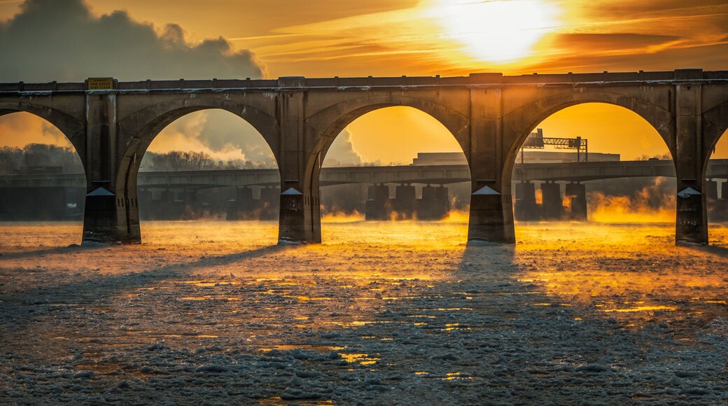 A bridge with multiple arches over a body of water during sunset.