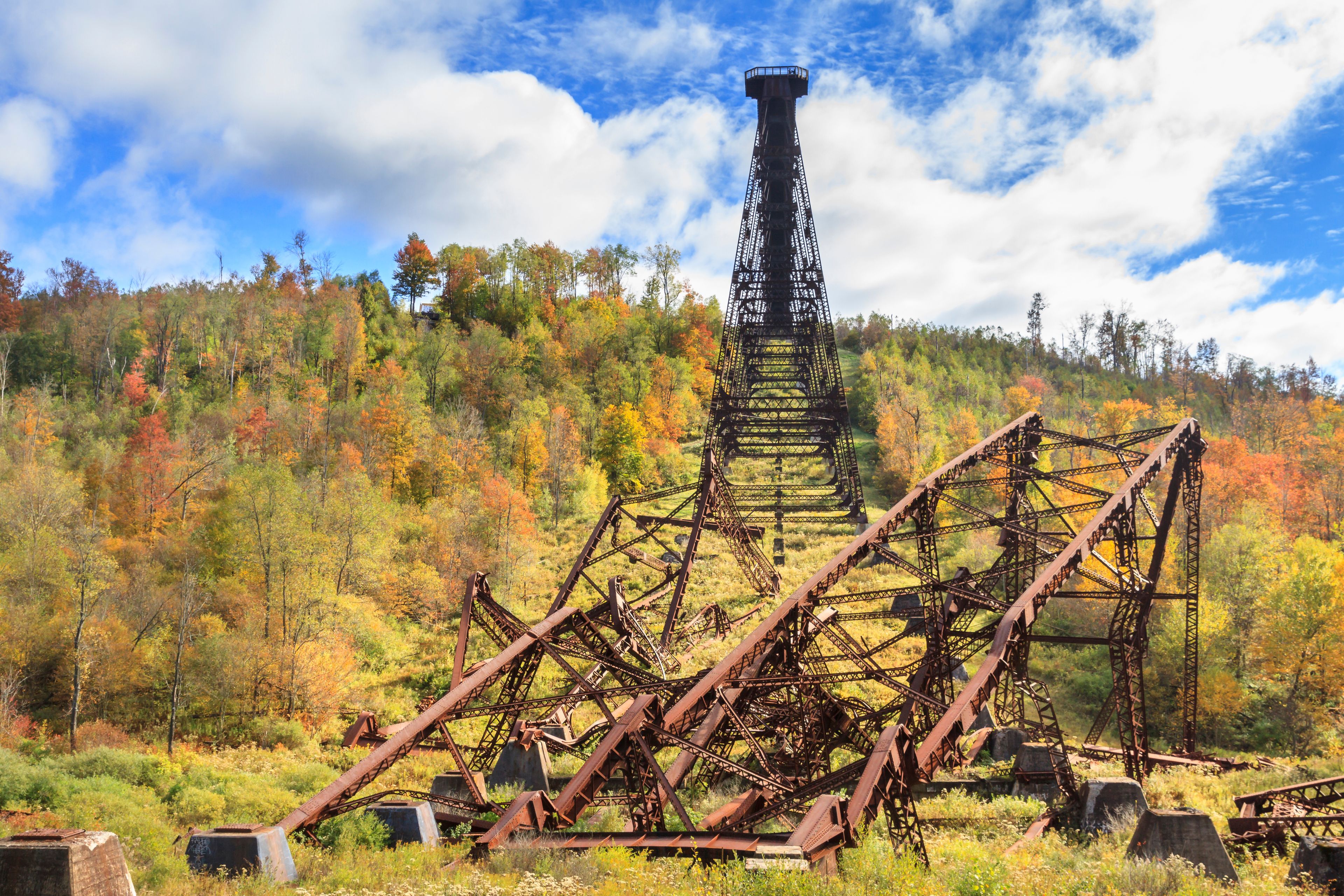 A rusted metal structure with a tower, surrounded by autumn-colored trees.