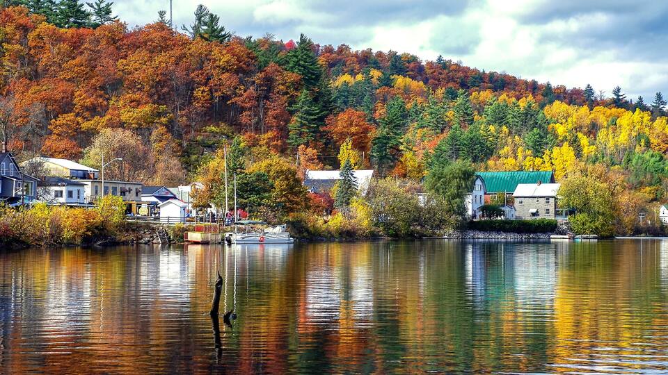 A lake with autumn foliage, houses, and a dock.