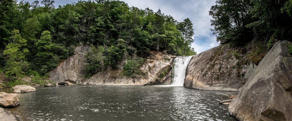 A waterfall cascading into a calm pool surrounded by rocky terrain and dense forest.