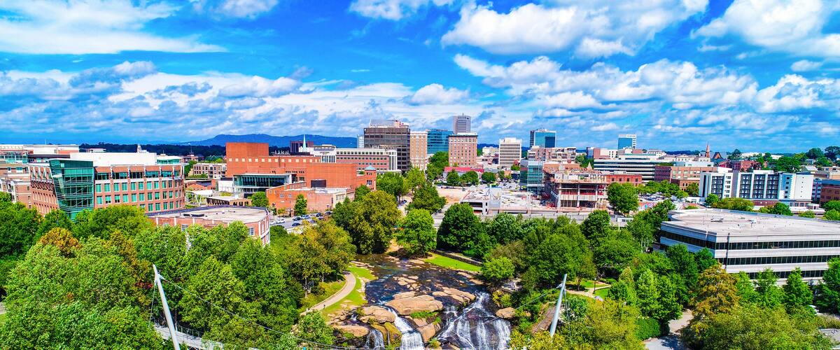 A cityscape with a waterfall, green trees, and modern buildings.