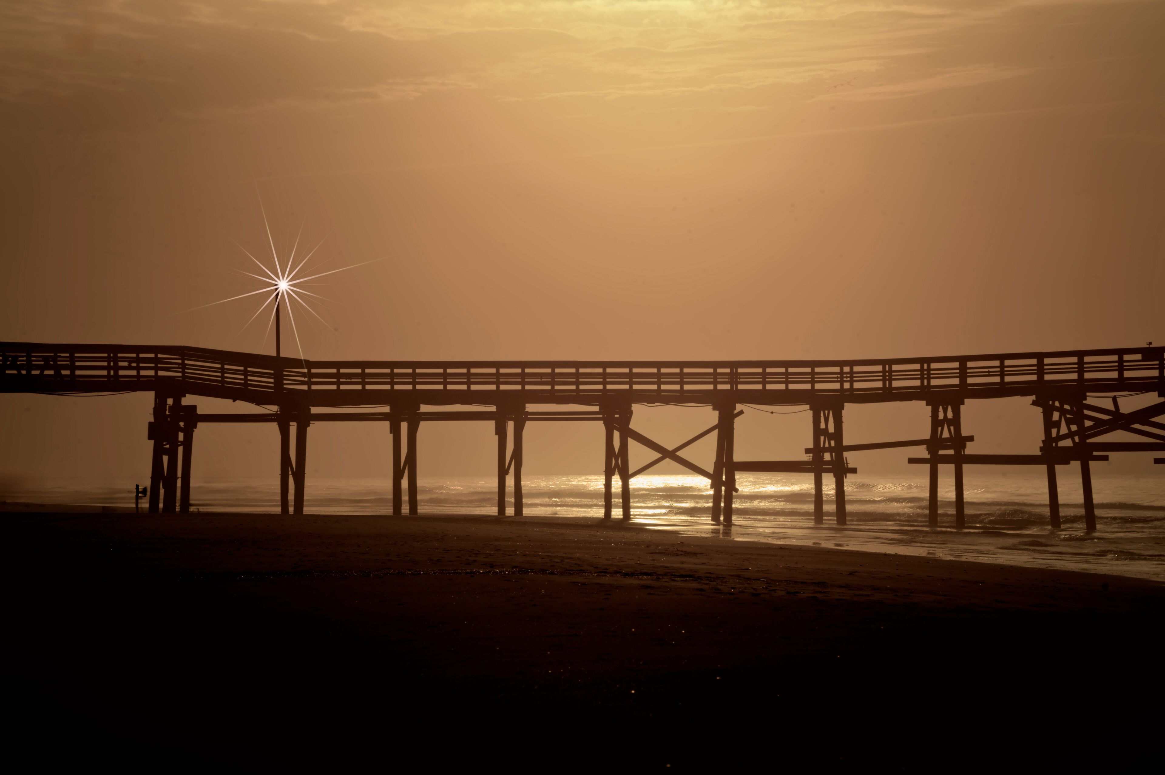 
Cherry Grove Fishing Pier The image shows a serene sunrise scene at North Myrtle Beach, South Carolina. A wooden pier stretches across the frame, extending out over the calm ocean waters. 