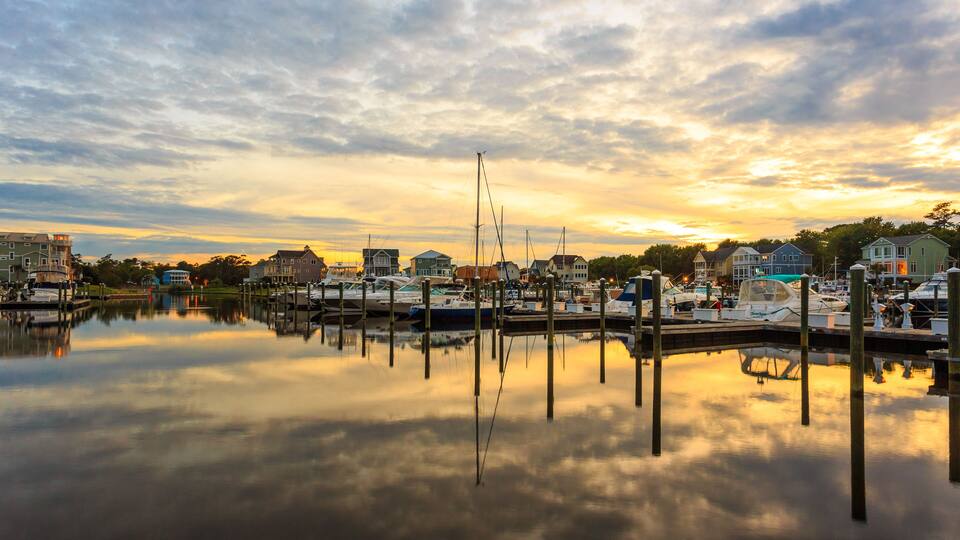 A marina with boats docked, surrounded by houses and a sunset sky.